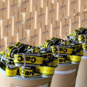 Drums filled with rolled yellow “Cargo” tie-down straps in front of stacked SBIA cardboard boxes.