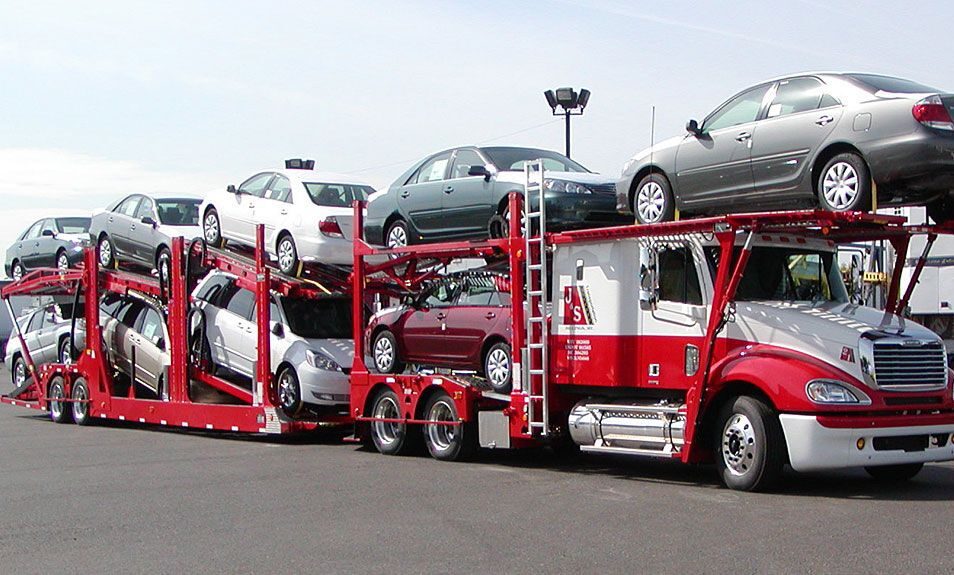 Red car hauler truck trailer loaded with multiple vehicles for transport