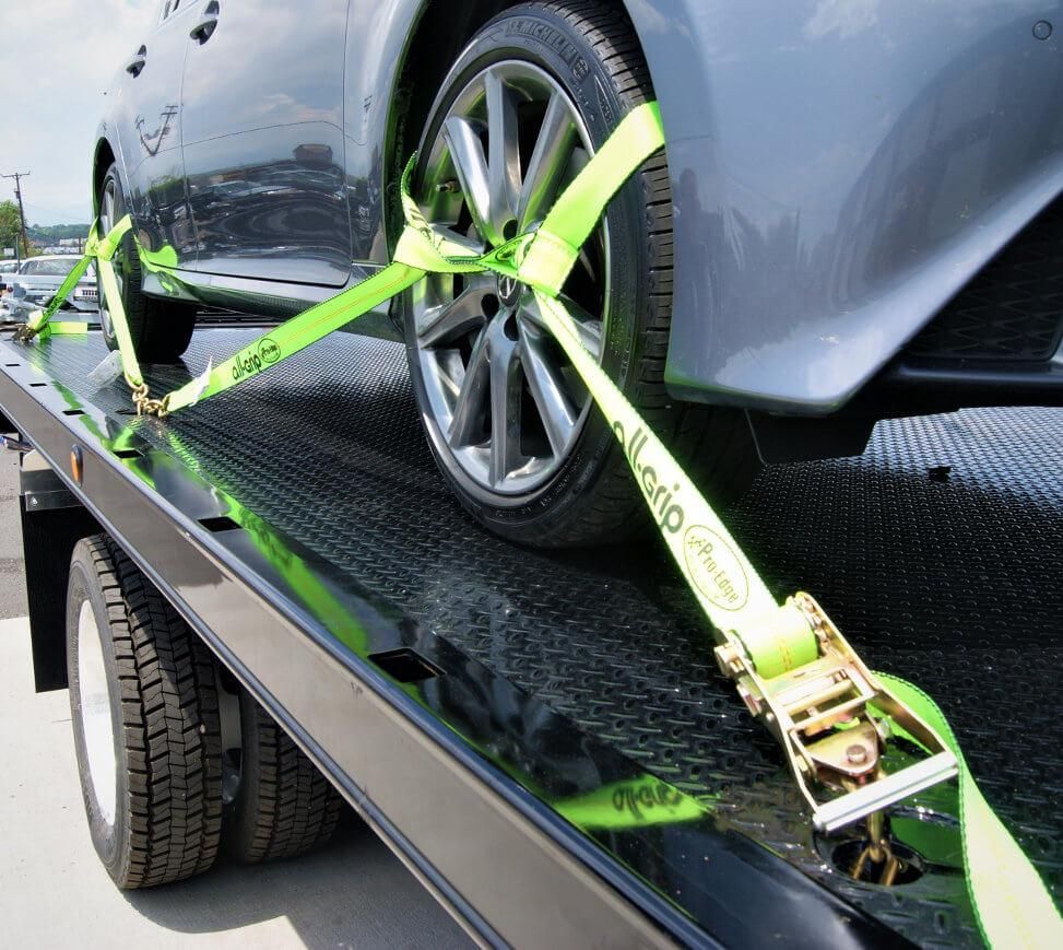 Car secured on flatbed with neon green wheel straps and ratchet tie-downs