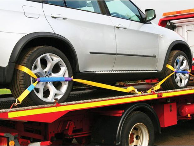 Car secured on flatbed tow truck with wheel tie-down straps